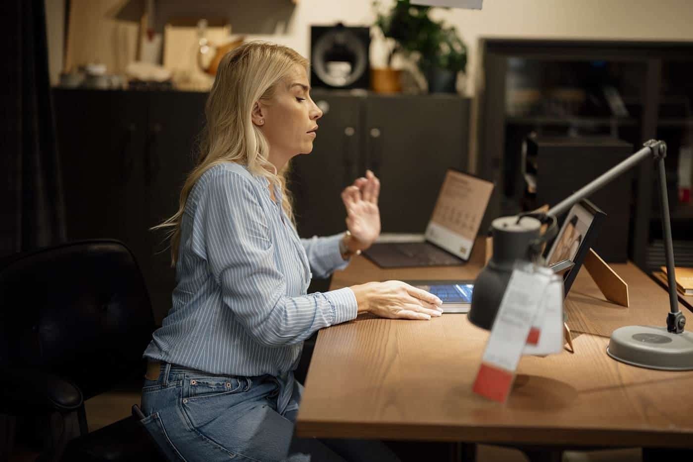 A woman working at a laptop on a wooden desk in a home office