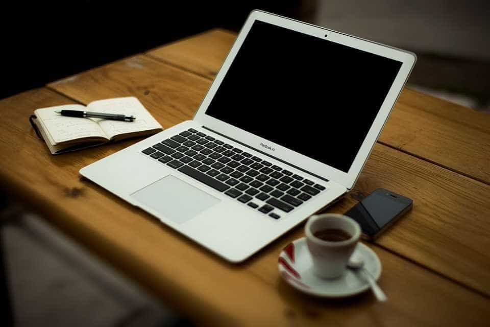 A laptop, notebook, phone and cup of coffee on a wooden desk